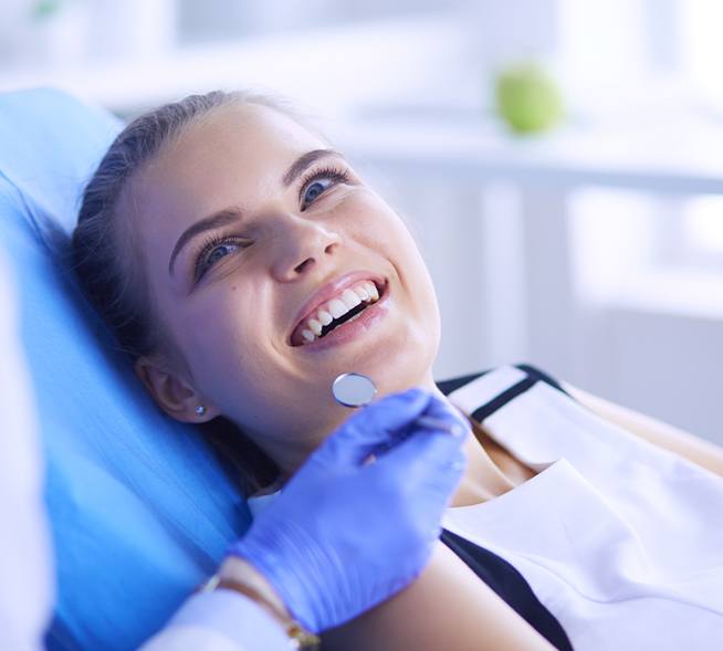 Woman in dental chair smiling up at dentist