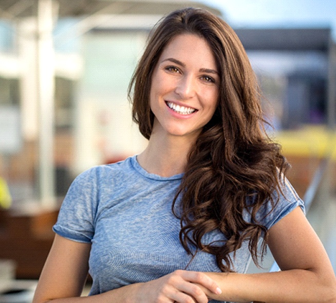 A young woman propping her elbow up on a railing while standing outside and smiling after an appointment with her female dentist in Mt. Dora