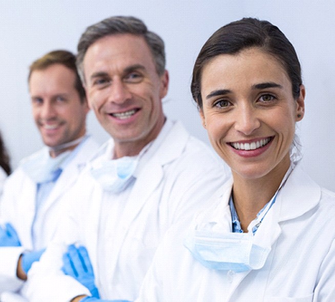 A row of dental professionals standing in a line wearing personal protective equipment and smiling