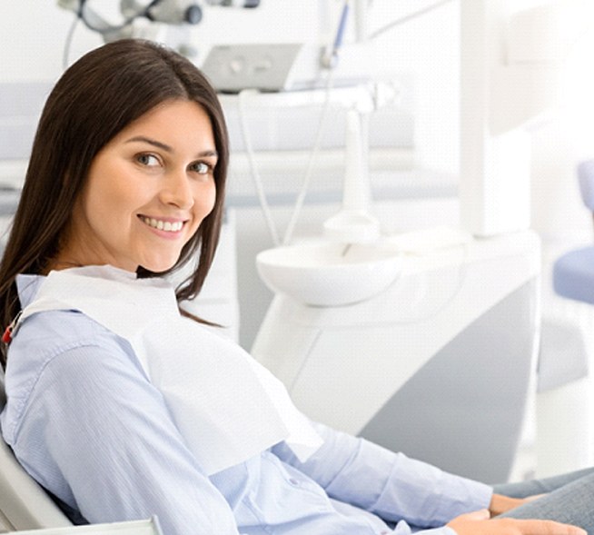 A young female with dark hair sitting back in the dentist’s chair and smiling in preparation for an appointment