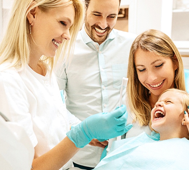 A young girl sitting in her mother’s lap while the father looks on as a female dentist in Mt. Dora explains how to properly brush