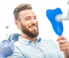 Man smiling while looking at reflection in tooth-shaped mirror