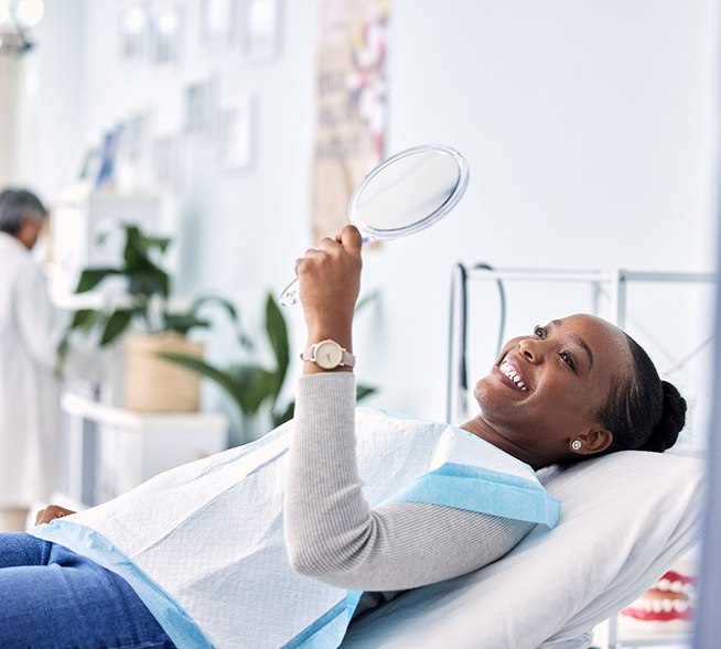 Woman smiling at reflection in handheld mirror