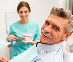 An older man smiles while his dental hygienist explains the process of receiving dental implants and how to properly care for them