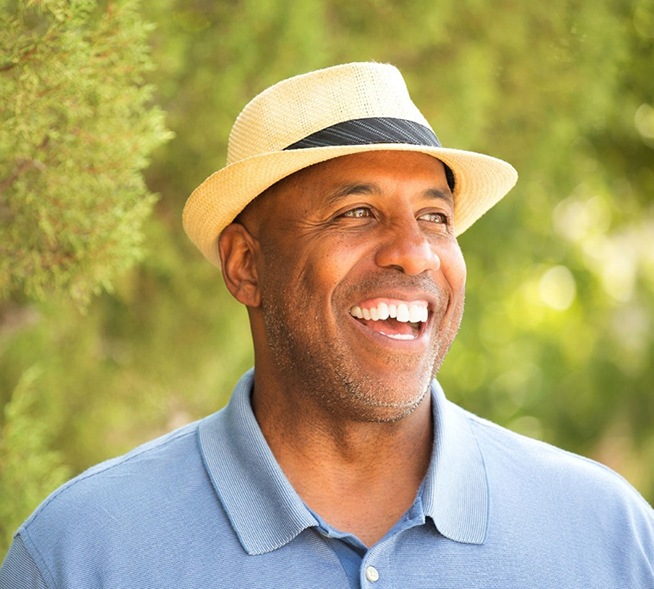 smiling man wearing a fedora and blue polo shirt 