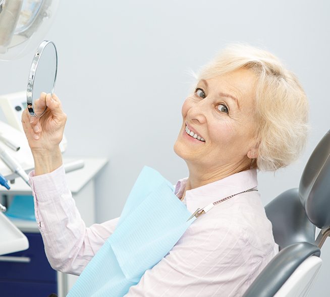Older woman in dental chair looking at her new denture