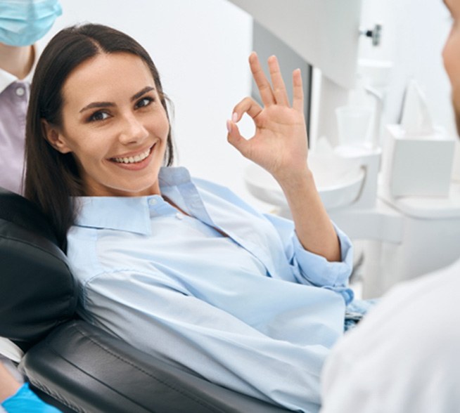 Patient in dental chair smiling giving OK hand sign