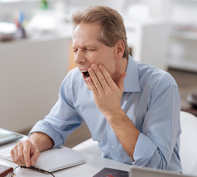 Man in need of T M J therapy holding jaw in pain