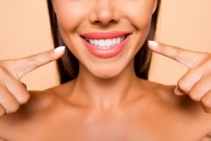 Woman pointing to her smile after receiving cosmetic dentistry.