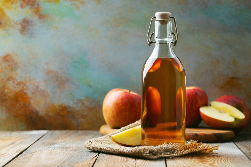 Apple cider vinegar in clear container next to sliced apples