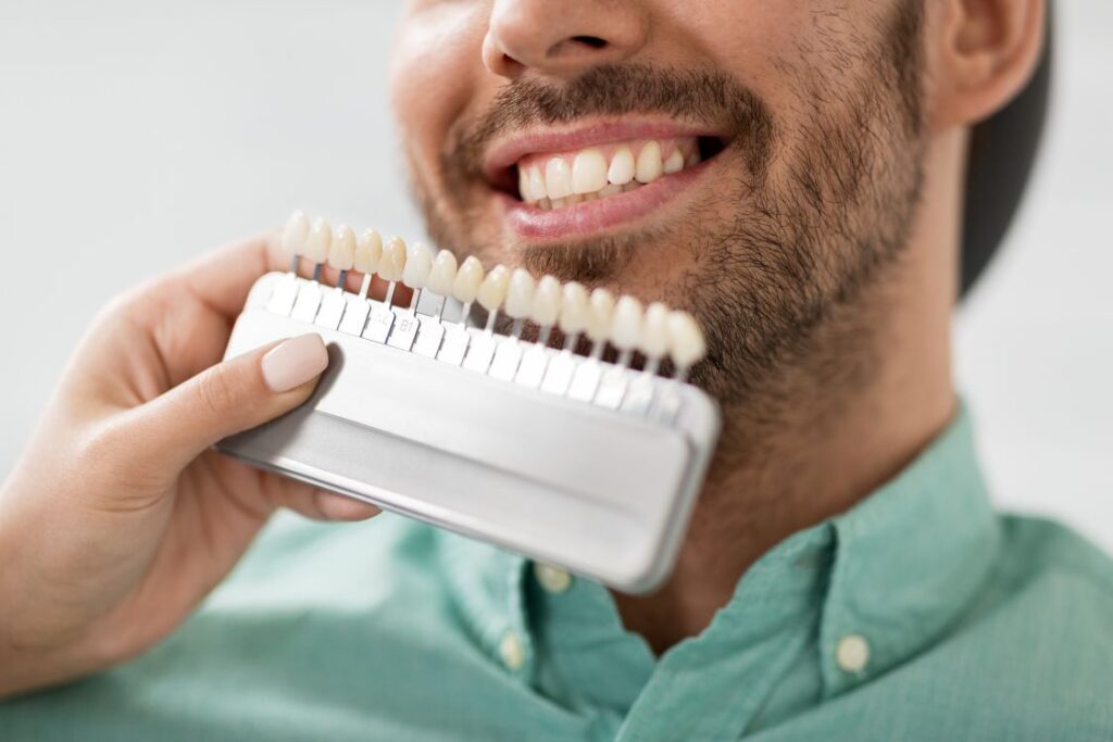 A man’s teeth next to a tooth shade indicator